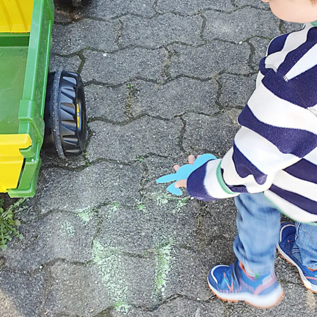 Kind entdeckt eine Hasenspur aus Kreide auf dem Boden als Hinweis für eine Osternest-Suche für Kleinkinder im Garten.
