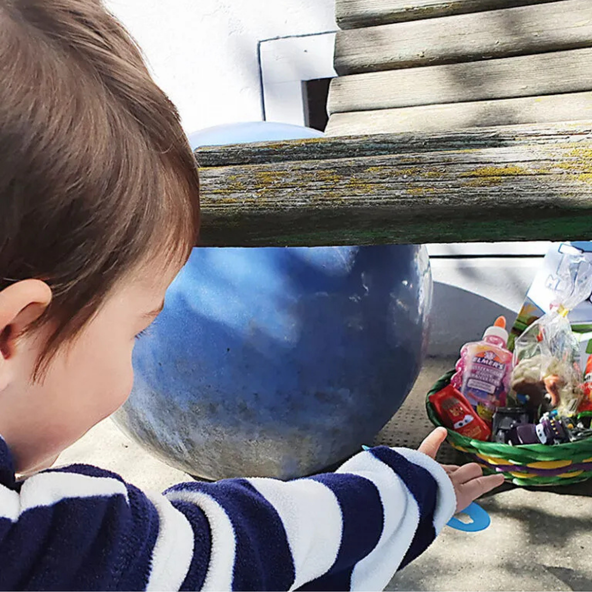 Kleinkind entdeckt ein verstecktes Osternest mit kleinen Geschenken im Garten während einer Osternest-Suche.